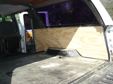 1992 Ford C-350 (Centurion Conversions) - The interior of a vehicle shows unfinished plywood paneling on the side wall and a dark, dusty floor.