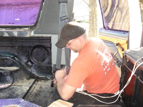 1992 Ford C-350 (Centurion Conversions) - Man works on wiring inside a vehicle's rear compartment, with a purple tinted window visible.