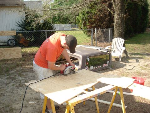 1992 Ford C-350 (Centurion Conversions) - A person works on cutting plywood next to a truck cap with several stickers on its rear window.