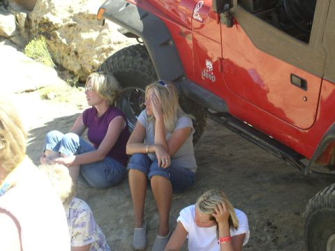 1979 Ford Bronco - A red Jeep Wrangler is parked on a rocky surface while several people sit on the ground next to it.
