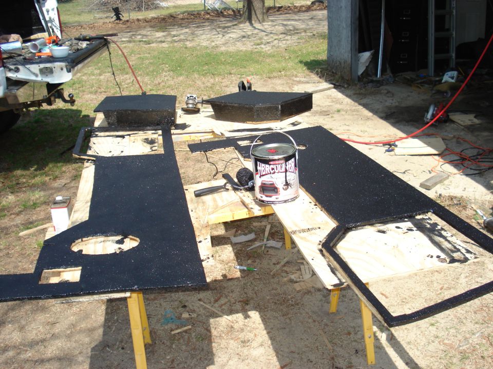 Vehicle interior panels coated in black material, with a can of Hercules coating and tools nearby. Part of a truck bed is visible