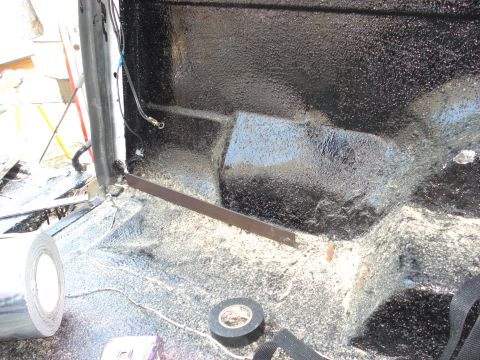 1992 Ford C-350 (Centurion Conversions) - The interior floor of a vehicle is covered in black spray-on liner, with rolls of tape and wiring visible.
