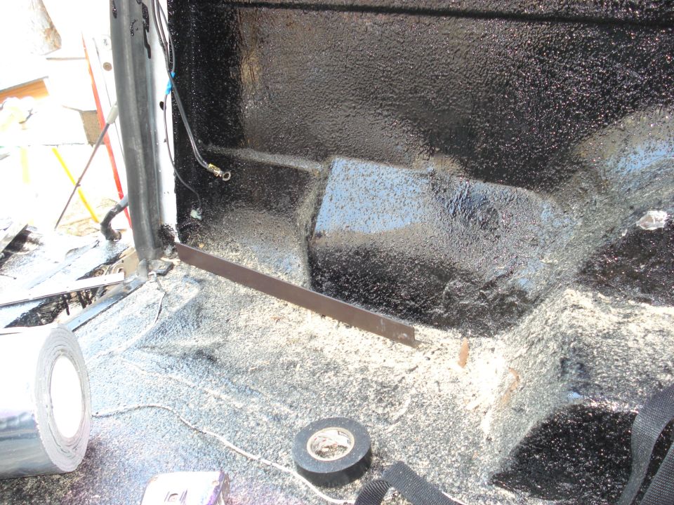 Interior floor of a vehicle with black spray-on bed liner and some tools like tape rolls