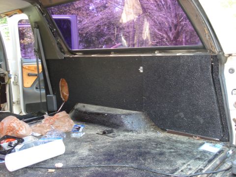 1992 Ford C-350 (Centurion Conversions) - The interior of a vehicle shows a rough textured wall panel and a floor covered in debris, with tinted windows in the background.