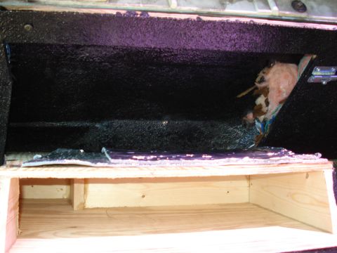 1992 Ford C-350 (Centurion Conversions) - Interior of a shop-built storage compartment with a raw plywood box frame below and an upper cavity sprayed with thick black textured bedli…