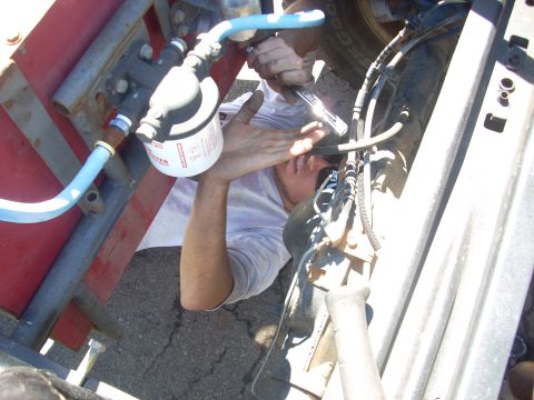 1992 Ford Ranger - A mechanic works on the underside of a vehicle, focusing on a fuel filter and various hoses and lines.