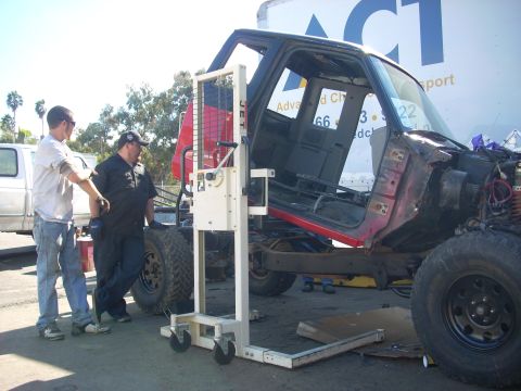 1992 Ford Ranger - A truck cab is being moved by a lift, with two men observing the process. A trailer with the ACT logo is visible in the background.