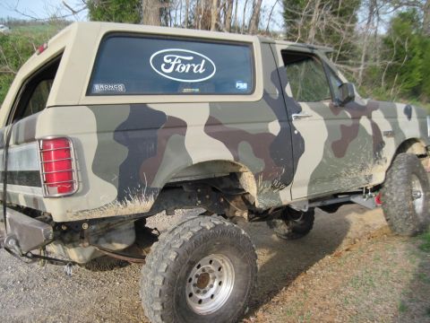 1995 Ford Bronco - Camouflaged 1995 Ford Bronco parked on a dirt road.