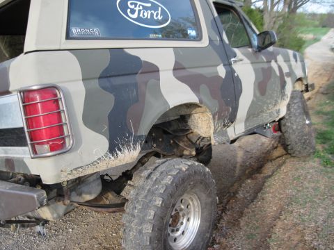 1995 Ford Bronco - This Ford Bronco is shown from the rear quarter angle, driving on a dirt road with camouflage paint.