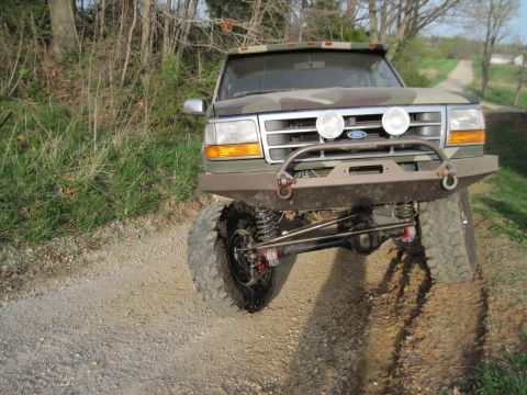 1995 Ford Bronco - A lifted Ford Bronco with a camouflage paint scheme is shown from the front on a dirt path.