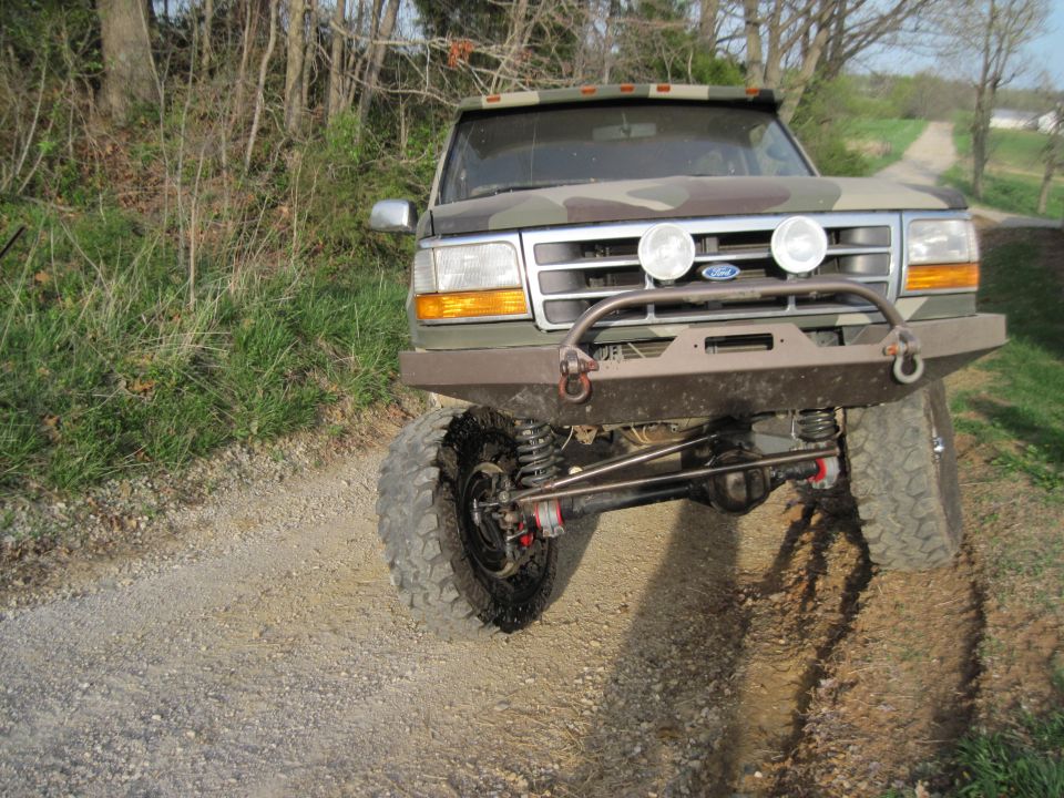 Camouflaged Ford Bronco with lifted suspension and off-road bumper on a dirt road