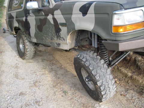 1995 Ford Bronco - Camouflaged 1995 Ford Bronco on a dirt path, showing off its lifted suspension and off-road tires.