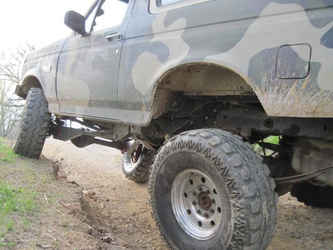 1995 Ford Bronco - This lifted Ford Bronco, painted in camouflage, is equipped with large off-road tires and appears to be on a dirt trail.