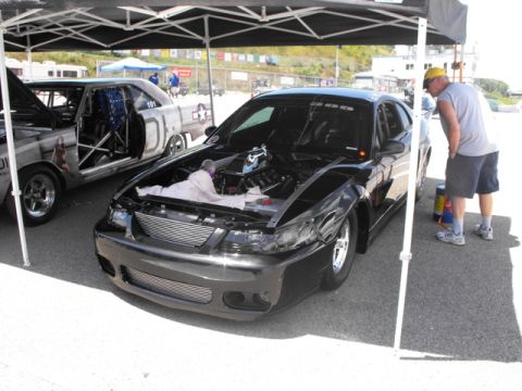 1992 Ford Mustang - Two cars are parked under a canopy at what appears to be a race track event.