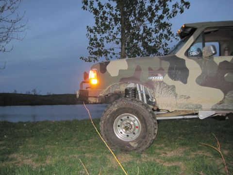 1995 Ford Bronco - A lifted, camouflaged Ford Bronco sits near a lake at dusk.