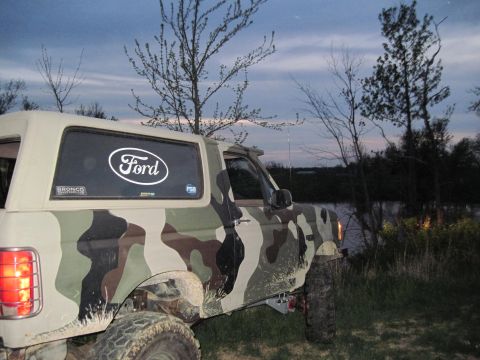 1995 Ford Bronco - A 1995 Ford Bronco sports a camouflage paint job and is parked outdoors near a body of water.