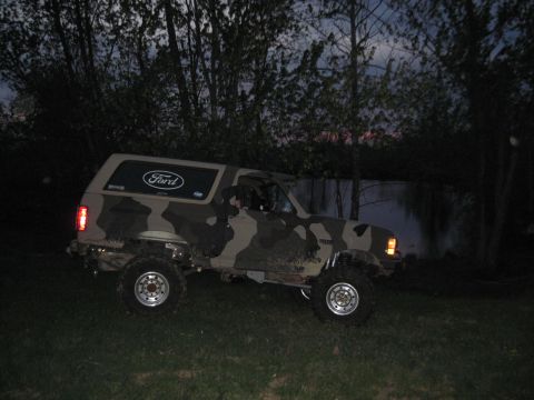 1995 Ford Bronco - This Ford Bronco has a camouflage paint scheme and is parked on grass with trees in the background.