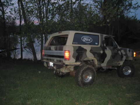 1995 Ford Bronco - A camouflaged Ford Bronco is parked on a grassy area next to a body of water at dusk.