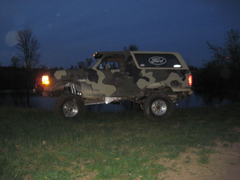 Camouflaged Ford Bronco with lifted suspension and off-road tires, viewed from the side at dusk