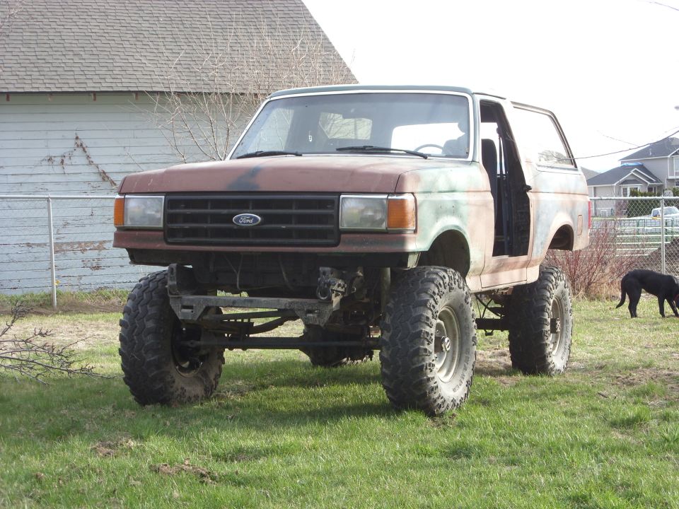 Modified Ford Bronco with large tires and lifted suspension, doors removed. Camouflage paint scheme