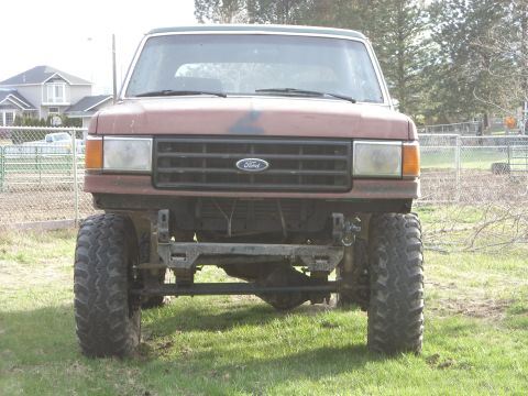 1988 Ford Bronco - This lifted Ford Bronco is parked on a grassy area with houses in the background.