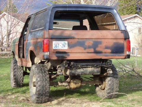 1988 Ford Bronco - This heavily modified Ford Bronco shows significant rust and camouflage paint. Rear view.