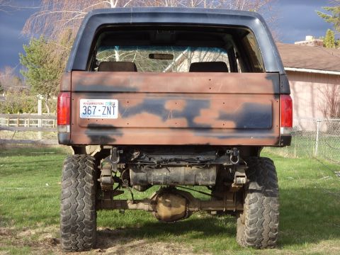 1988 Ford Bronco - This lifted Ford Bronco has a camouflage paint job and is parked on a grassy area with a house in the background.
