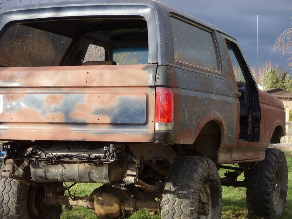 Rusty black Ford Bronco with lifted suspension and large tires, viewed from the rear