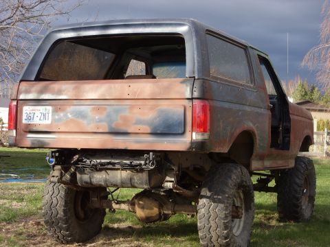1988 Ford Bronco - This heavily modified SUV features a lifted suspension and large off-road tires, with visible rust and missing body panels.