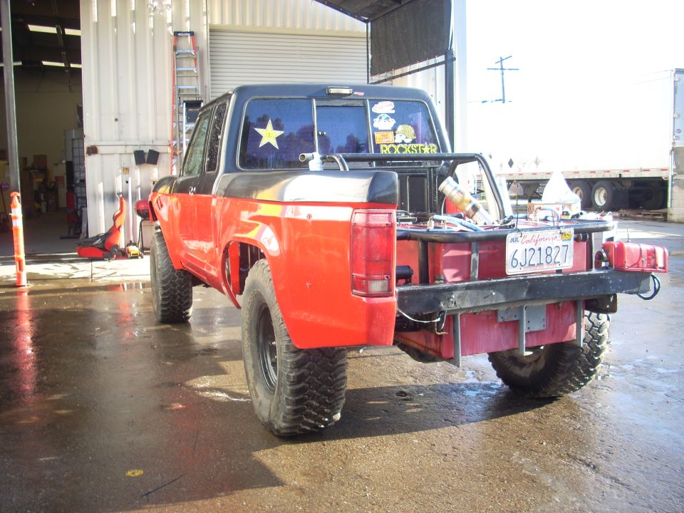 Red and black 1992 Ford Ranger pickup truck with custom flatbed, off-road tires, and aftermarket bumper