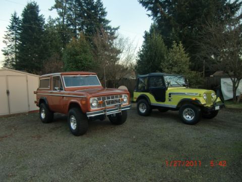 1973 Ford Bronco - Two classic off-road vehicles, a 1973 Ford Bronco and a Jeep CJ, are parked side-by-side in a driveway.