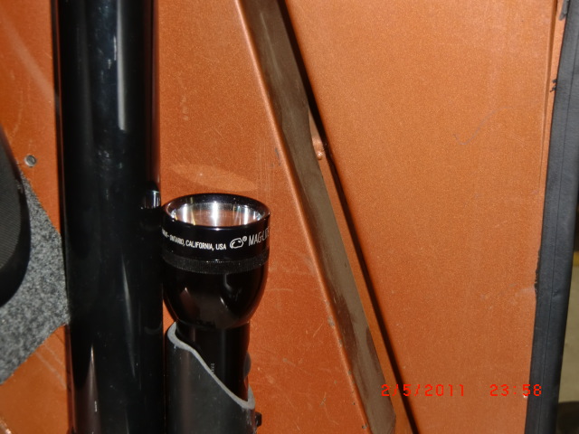 Black Maglite flashlight in a mount inside an orange vehicle. Text on flashlight reads 'Maglite, Ontario, California, USA'