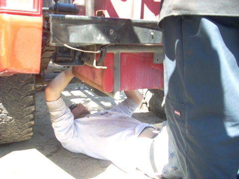 1992 Ford Ranger - A mechanic works on the underside of a red truck, with a focus on the frame and suspension components.