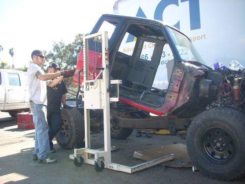 1992 Ford Ranger - A red truck cab is being lifted by a machine, with a white truck visible in the background.