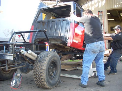 1992 Ford Ranger - Workers lift a truck cab during a cab swap operation, revealing the chassis and large tires.