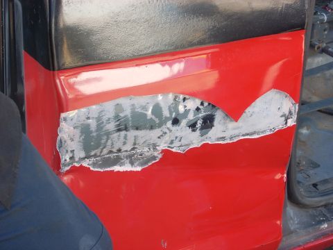 1992 Ford Ranger - This red truck door shows significant rust and damage, revealing exposed metal beneath the paint.