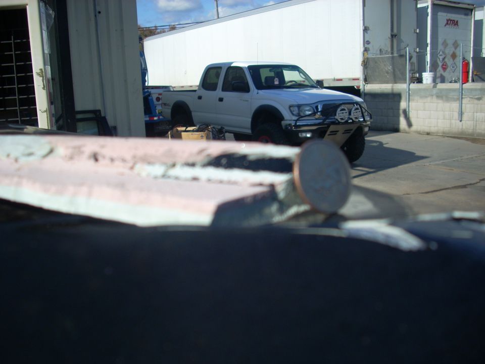 White Toyota Tacoma pickup truck with aftermarket bumper and lights parked near a loading dock