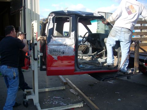 1992 Ford Ranger - A 1992 Ford Ranger cab is lifted by a machine, revealing its interior and damaged bodywork.