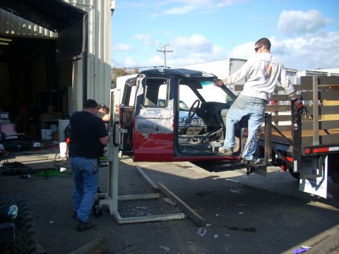 1992 Ford Ranger - Two men are working to load a truck cab onto a flatbed trailer using a lift.