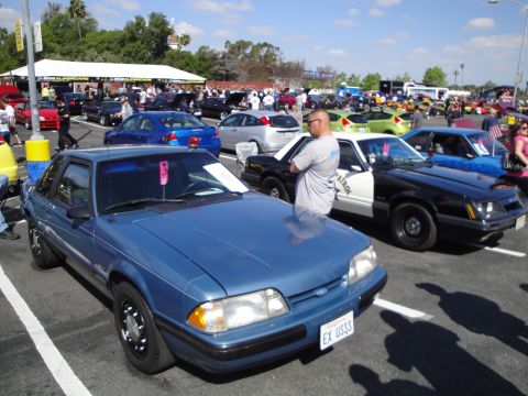 1993 Ford Taurus - A blue coupe is parked at an outdoor event with other vehicles and people around.