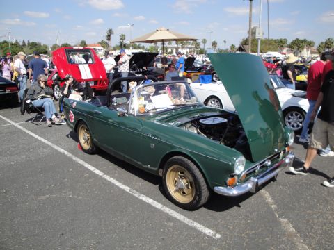 1993 Ford Taurus - Outdoor car show scene with a green convertible's hood open, surrounded by other vehicles and attendees.