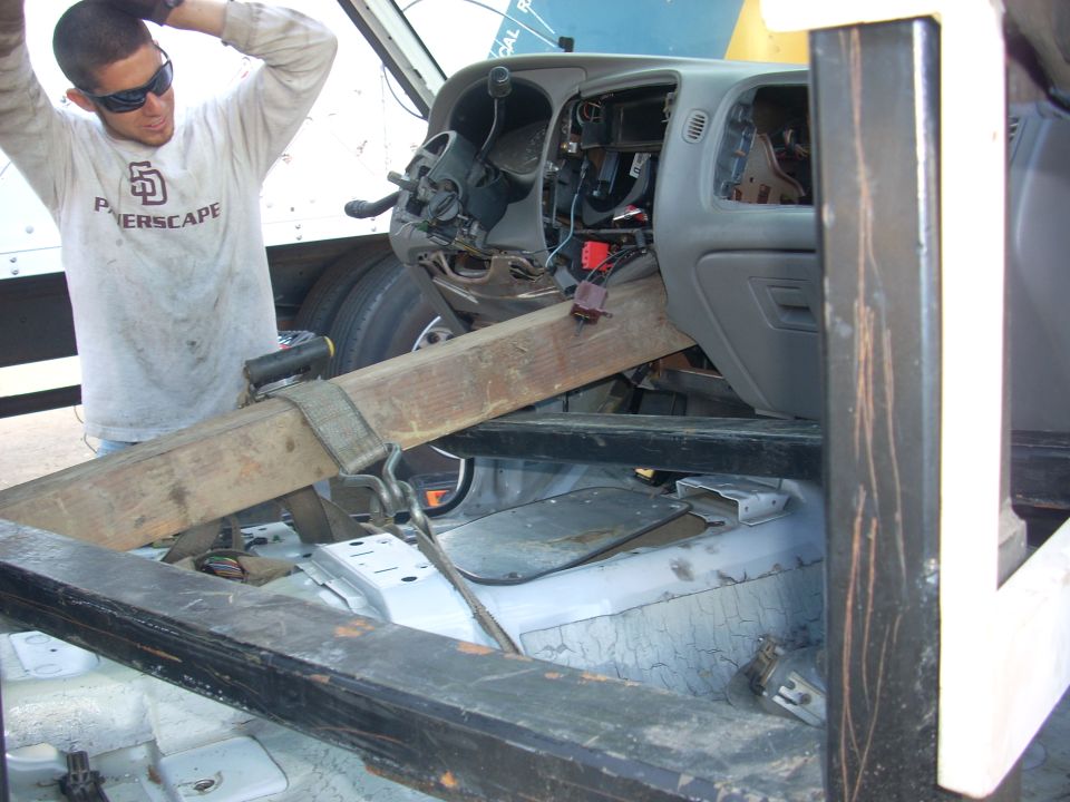 Interior of a disassembled truck cab with a man working on the dashboard