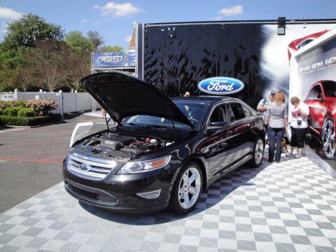 1993 Ford Taurus - A black Ford sedan is displayed with its hood open, next to a trailer with a Ford logo.
