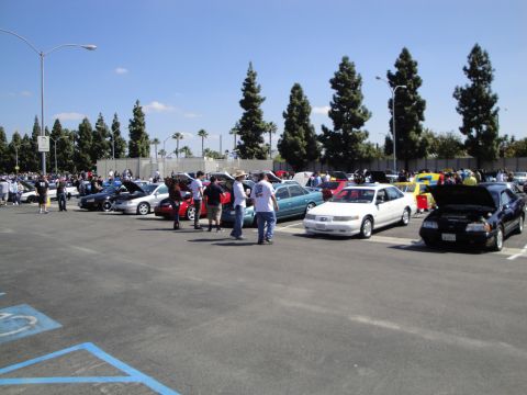 1993 Ford Taurus - A gathering of vehicles and people in an outdoor parking lot on a sunny day.