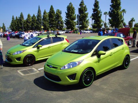 1993 Ford Taurus - Two lime green Ford Fiesta hatchbacks are parked side-by-side in an outdoor lot on a sunny day.