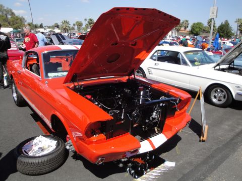 1993 Ford Taurus - An orange 1965 Ford Mustang is displayed with its hood open, revealing the engine compartment. A spare tire rests on the ground nearby.