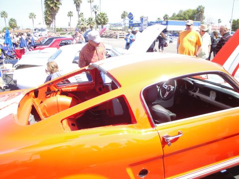 1993 Ford Taurus - An orange classic car is displayed at an outdoor event with other vehicles and people.