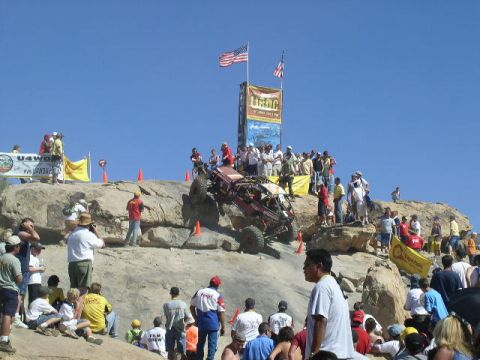 1979 Ford Bronco - A crowd watches as a custom off-road vehicle navigates a challenging rocky terrain under a clear blue sky.