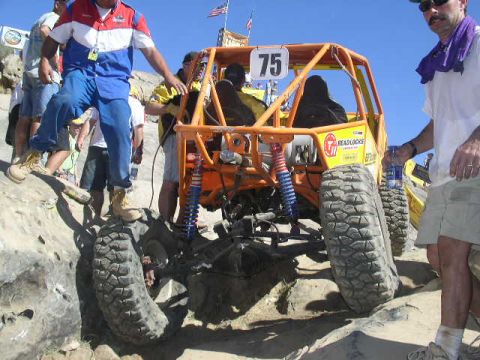 1979 Ford Bronco - An orange off-road buggy with number 75 on its roof is shown tackling a challenging rocky course.