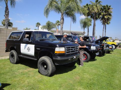 1993 Ford Taurus - Several modified trucks and SUVs are parked on a grassy field under palm trees on a sunny day.